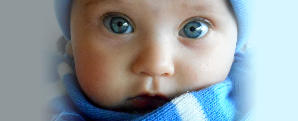Bebé con ojos azules grandes tiene un gorro y una bufanda azul y blanca.